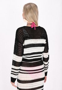 Randig stickad tröja i svart, vitt och rosa. Har långa ärmar, öppen vävstruktur och en V-hals med en rosa knytning.