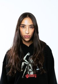 Sudadera negra con capucha que presenta una impresión gráfica de una figura con los brazos extendidos y acentos rojos. Tejido suave con un corte relajado.