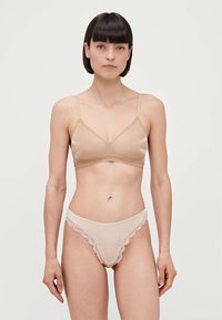 Nahat bralette ja sobiv thong siledast kangast. Bralette'il on õhukesed rihmad ja kolmnurkne kuju; thongil on puuvillane ääris vöökoha ümber.