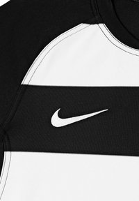 Zwart-wit Nike sportshirt met horizontale strepen, ronde halslijn en geborduurd logo op de bovenste linkerkant. Zachte textuur.