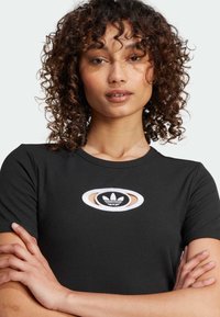 Czarny rypsowy t-shirt z białym i czarnym haftowanym logo Adidas w owalnym kształcie na klatce piersiowej. Krótkie rękawy i okrągły dekolt.