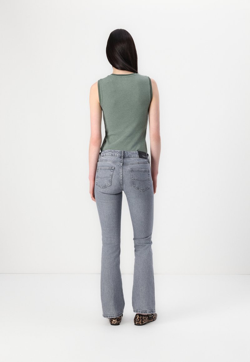 Top senza maniche a righe verdi abbinato a jeans grigi chiari a campana, con tasche posteriori e un'etichetta nera sulla cintura. Scarpe con stampa animale.