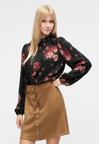 Blusa negra plisada con estampado floral y mangas largas, combinada con una minifalda de ante color canela con cierre frontal de botones y textura suave.