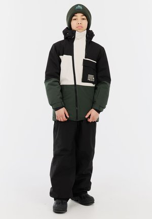 Schwarz-weiße und grüne Jacke mit einem Reißverschluss und einer Fronttasche; kombiniert mit schwarzen Hosen und Schuhen; weiche Textur; legere Outdoor-Bekleidung.