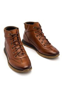 Brązowe skórzane botki za kostkę o strukturalnym wykończeniu, z wiązaniem i wyściełanym kołnierzem. Posiadają subtelne szwy i gumową podeszwę dla lepszej przyczepności.