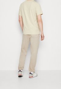 Beżowa bawełniana koszulka z okrągłym dekoltem, w zestawie z beżowymi spodniami dresowymi. Charakteryzuje się subtelną teksturą oraz sportowymi butami w odcieniach szarości, bieli i czerwieni.