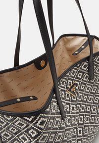 Black and white patterned tote bag with synthetic exterior, gold hardware, and a beige interior featuring a logo print. Double shoulder straps.