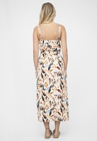 Maksimekko, jossa säädettävät ohuet hihnat, kuvioitu lämpimissä oranssin, beigen ja mustan sävyissä; vyötäröltä kapeaksi somistettu, laskeutuvaa kangasta.