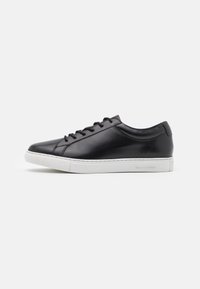 Black leather sneaker with a rounded toe, minimal lacing, and a white rubber sole. Features subtle branding on the side. Smooth texture.