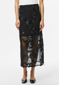 Jupe noire avec broderies florales, superposée sur un matériau transparent. Taille élastique, longueur cheville, avec des motifs floraux détaillés.