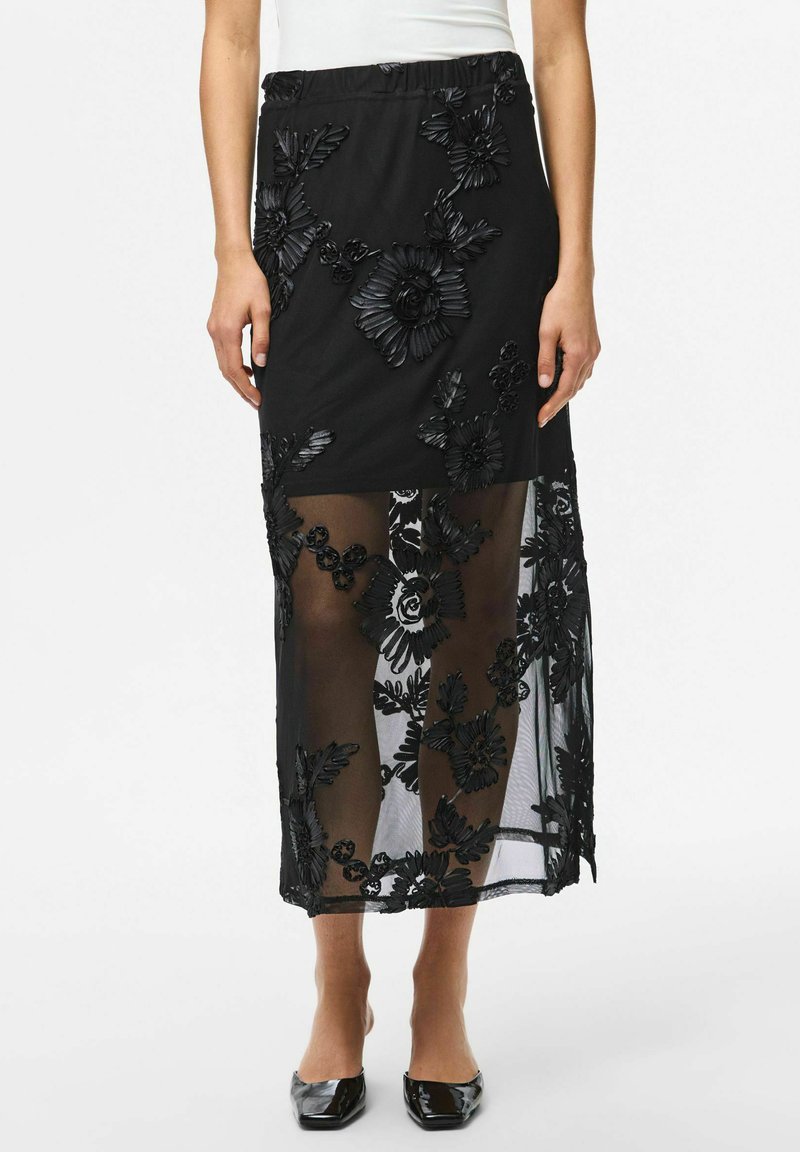 Jupe noire avec broderies florales, superposée sur un matériau transparent. Taille élastique, longueur cheville, avec des motifs floraux détaillés.