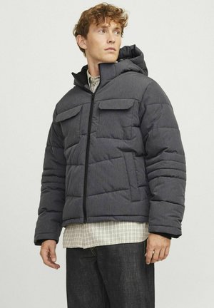 Gray puffer jacket with a textured finish, featuring a hood, zip front, and two chest pockets. Worn over a plaid shirt.