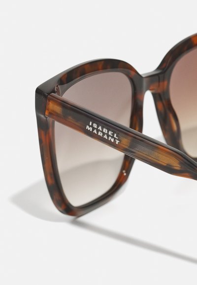 Γυαλιά ηλίου από σκληρό υλικό σε χρώμα χελώνας με χοντρό, γωνιακό σκελετό. Φακοί με κλίση σε καφέ απόχρωση, με την επιγραφή "Isabel Marant" ανάγλυφη στον βραχίονα.