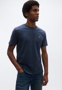 Granatowy bawełniany t-shirt z okrągłym dekoltem, krótkimi rękawami i małym haftowanym logo na piersi, zestawiony z dżinsami.