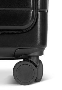 Eck eines schwarzen Koffers mit glatter, strukturierter Oberfläche, robustem Reißverschluss und zwei runden schwarzen Rollen für Mobilität.