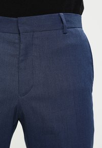 Mörkblå dressbyxor med en strukturerad, vävd mönstring. Funktioner en rak front, sidofickor och slim fit. Skräddarsydd midjedetalj.