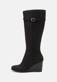 Bottes hautes jusqu'au genou en daim noir avec un talon compensé, présentant une boucle latérale décorative et une texture lisse.
