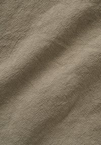 Gros plan sur un tissu en lin beige montrant la texture tissée détaillée et des plis naturels subtils.