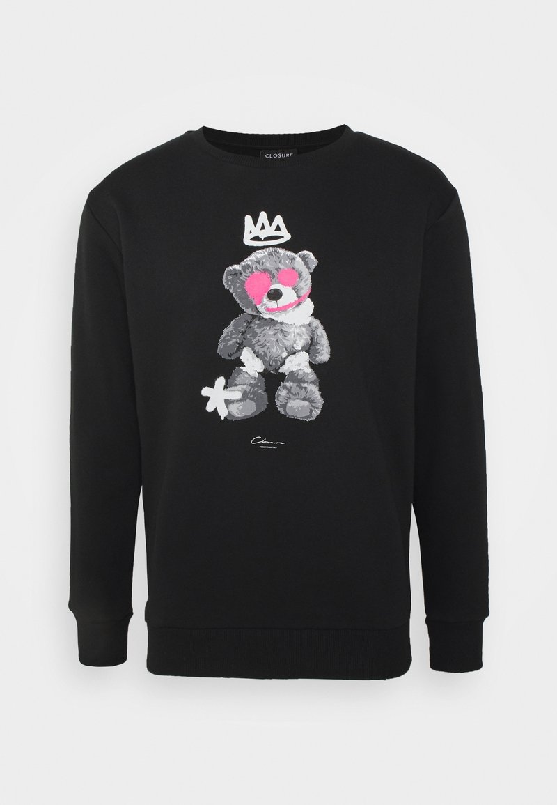 Sweatshirt noir avec un graphisme d'ourson gris, un œil et une joue peints en rose, une couronne blanche au-dessus, et une marque blanche ressemblant à une fleur près de son pied.