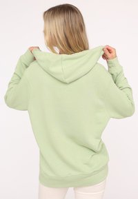 Haut à capuche vert clair en tissu doux, doté d'une capuche avec cordon de serrage, de poignets côtelés et d'une coupe décontractée. Aucun motif ni graphique visible.