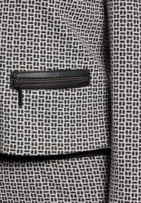 Tissu à motifs noir et blanc avec un design géométrique ; comporte une poche zippée avec une bordure en cuir noir. Surface texturée.