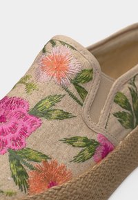 Chaussure à enfiler en tissu beige, semelle tissée, ornée de fleurs brodées colorées en rose, orange et feuilles vertes sur la tige.