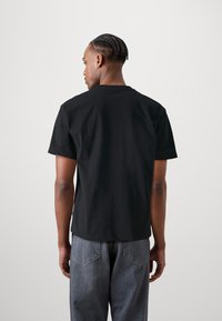 Camiseta negra de algodón con cuello redondo clásico, mangas cortas y un corte relajado, vista desde la parte de atrás contra un fondo liso.