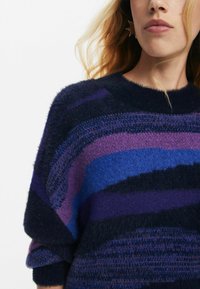 Paarse en blauwe gestreepte gebreide trui met een zachte, pluizige textuur. Heeft een ronde halslijn en omgeslagen mouwen, wat zorgt voor een ontspannen pasvorm.