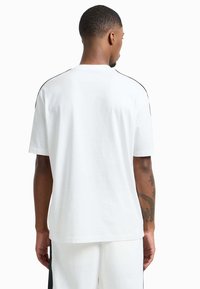 Witte katoenen t-shirt met korte mouwen, een ronde hals en zwarte accentstiksels langs de schoudernaden. Glad textuur.