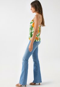 Camisola floral con patrón de hojas amarillas y verdes, combinada con jeans acampanados de lavado claro. Tela suave y ajuste ceñido. Diseño minimalista.