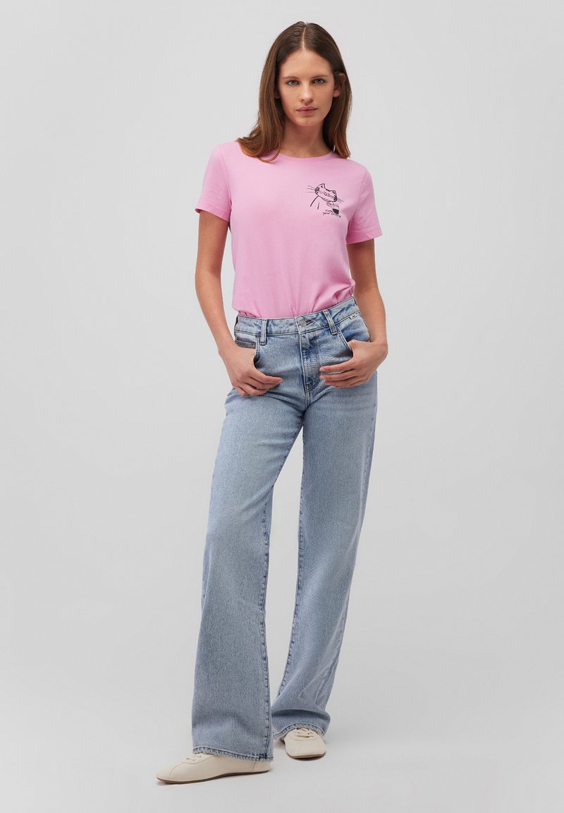 Pink cotton T-shirt with a black graphic design on the chest, paired with light blue wide-leg jeans, and beige sneakers.