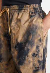 Shorts i ett brunt och svart tie-dye-mönster, tillverkade av ett lätt material med resårmidja och broderad logotyp på sidan.