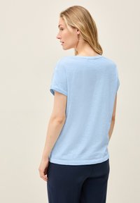 Camisa de manga corta azul claro con cuello redondo, hecha de una tela suave y texturizada. La camisa cuenta con mangas enrolladas y un ajuste relajado.