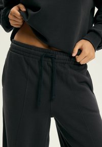 Czarne dresy z elastycznym pasem, detalem sznurkowym oraz bocznymi kieszeniami. Wykonane z miękkiego, teksturowanego materiału.
