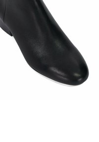 Bottine en cuir noir avec un bout pointu, texture lisse et un petit talon. Présente un design sans coutures et sans éléments visibles.