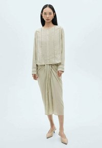 Top bej cu maneci lungi, cu placket și cusături decorative, asortat cu o fustă drapată. Țesătură fină și croială ajustată.
