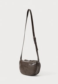 Geantă de tip crossbody din piele maro cu formă rotunjită. Are o curea lungă reglabilă și două buzunare frontale. Suprafață texturată cu un ușor luciu.