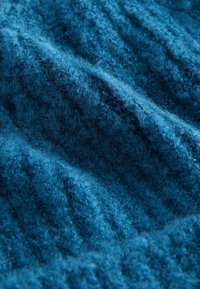 Tissu texturé bleu avec une apparence douce et duveteuse, présentant un motif nervuré et des nuances variées de bleu profond, créant de la profondeur.