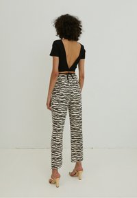 Černý, přiléhavý crop top s hlubokým V výstřihem na zádech, v kombinaci s vysokým pasem a vzorovanými kalhotami v béžové barvě s černými tygřími pruhy. Sandály na podpatku.