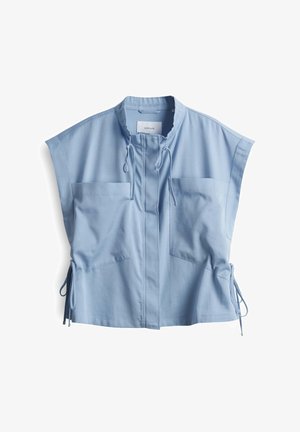 Lichtblauw mouwloos topje met hoge kraag, twee voorzakken, sluiting met trekkoord en verstelbare zijkanten voor een aanpasbare pasvorm.