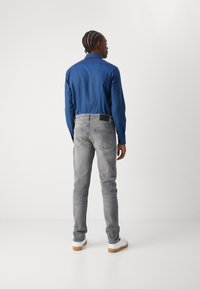 Camisa azul de manga larga combinada con jeans ajustados de color gris claro. Tejido texturizado con bolsillos traseros y detalle de etiqueta negra. Zapatillas blancas.