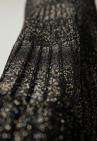 Svart tyg med glimmande guldprickar, med en plisserad textur som skapar en gradienteffekt. Närbild som betonar detaljer och mönster.