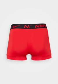 Șorturi sportive roșii cu un elastic negru la talie, având logo-ul "Nike" în roșu. Textură netedă cu un design ajustat.