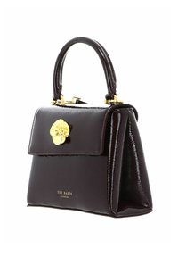 Sac à main en similicuir marron foncé au design structuré, avec quincaillerie dorée, une fermeture à motif floral et une anse unique sur le dessus. Nom de la marque visible en dessous.