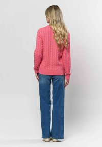 Lyserød kabelstrikket sweater med ribstrikkede manchetter og kant, parret med løse blå jeans. Blødt materiale og let løs pasform.