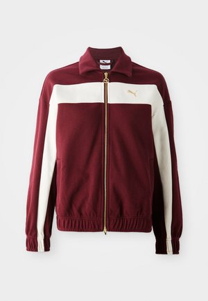 Bordeaux zip-jakke med hvide striber på ærmerne, guld lynlås og logo på brystet. Ribkant ved håndleddene og nederste kant med struktureret stof.