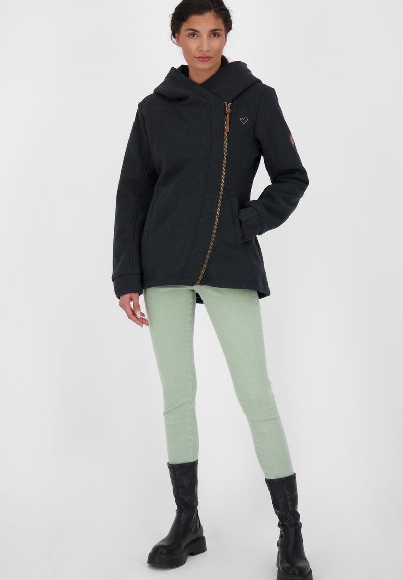 Czarna kurtka z kapturem, z ukośnym zamkiem i bocznymi kieszeniami; ma małe logo serca na piersi oraz przyjemny, fakturowany materiał.