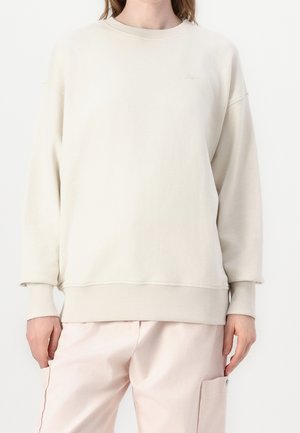 Person wearing an oversized cream sweatshirt with ribbed cuffs and hem, paired with light pink cargo pants, standing against a white background.