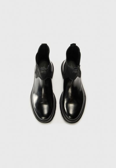 Bottines noires en cuir avec une finition lisse, panneaux latéraux élastiques et bout rond. Elles présentent un design minimaliste et une semelle texturée.