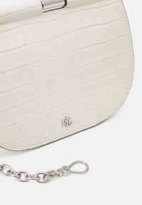 Vit, texturerad faux-krokodil läderhandväska med ett metallspänne och silverkedjestraps. Har en subtil logotyp på framsidan.